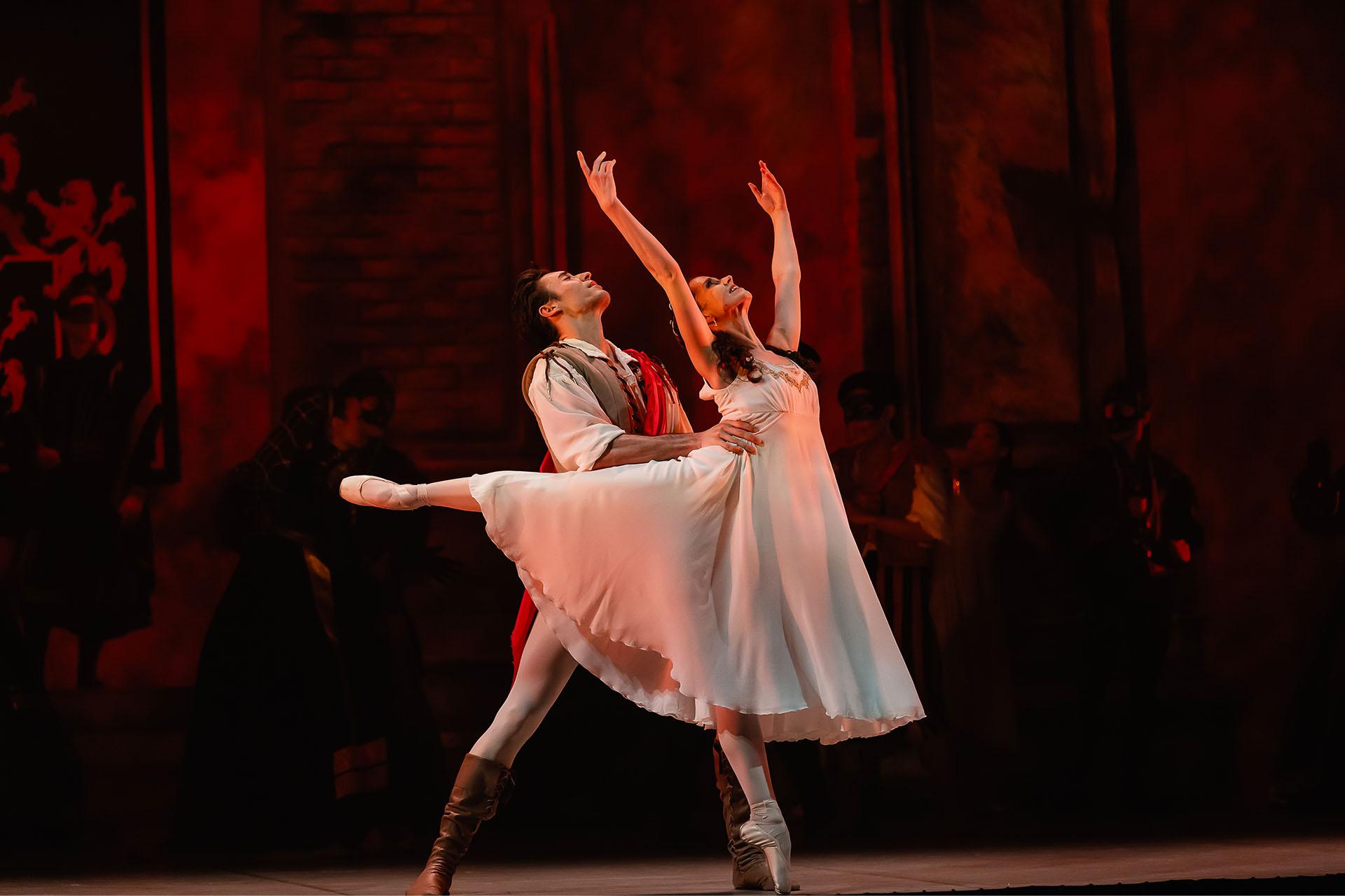 Juliet stands en pointe with her arms above her head, Romeo holds her by the waist