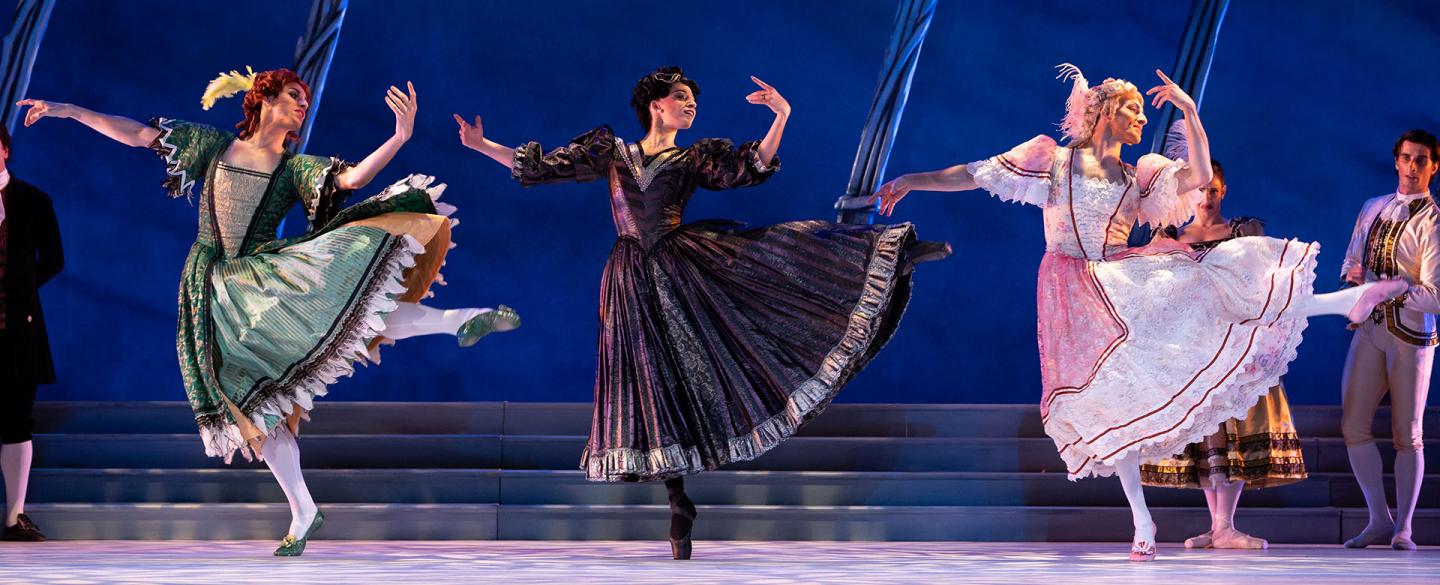 Three women, one in green, one in black, the other in pink, dance in unison